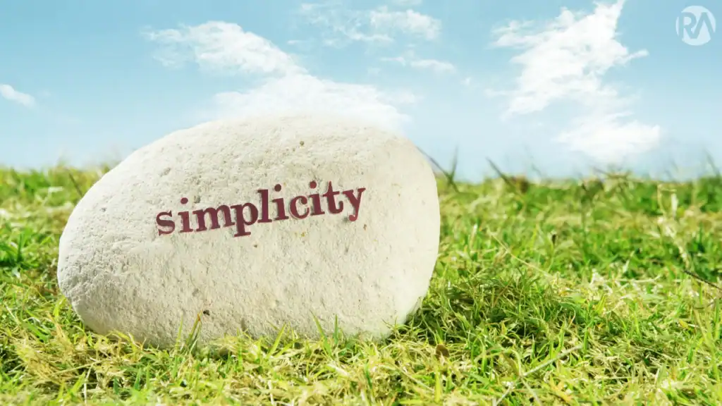 Simple stone with the word "simplicity" on grass under blue sky.